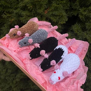 Op de afbeelding: Vijf gehaakte ratten speelgoed in een roze cadeaudoos. De ratten zijn bruin, grijs, zwart en wit. Ze hebben roze neuzen en snorharen.