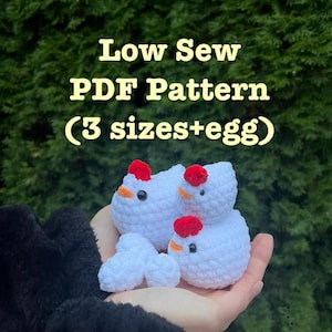 Puede incluir: Un grupo de pollos de ganchillo blancos con crestas rojas y picos naranjas, junto con un huevo de ganchillo, se muestran en una mano. El texto "Low Sew PDF Pattern (3 sizes+egg)" es visible en amarillo.