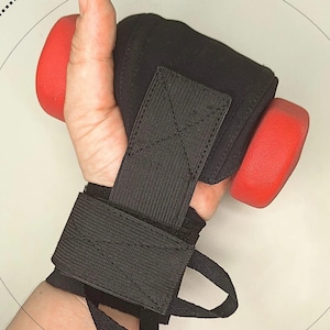 Può includere: Polsini neri per sollevamento pesi con un manubrio rosso. I polsini hanno una chiusura con cinturino sicura e sono progettati per fornire supporto durante gli allenamenti. L'immagine include anche il testo "A good grip".