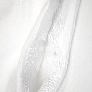 K&ouml;nnte beinhalten: Nahaufnahme eines wei&szlig;en Stoffes mit zwei transparenten Druckkn&ouml;pfen. Der Stoff scheint ein gewebtes Material zu sein, m&ouml;glicherweise Baumwolle oder Leinen, mit sichtbarer Textur. Die Druckkn&ouml;pfe sind gleichm&auml;&szlig;ig verteilt.