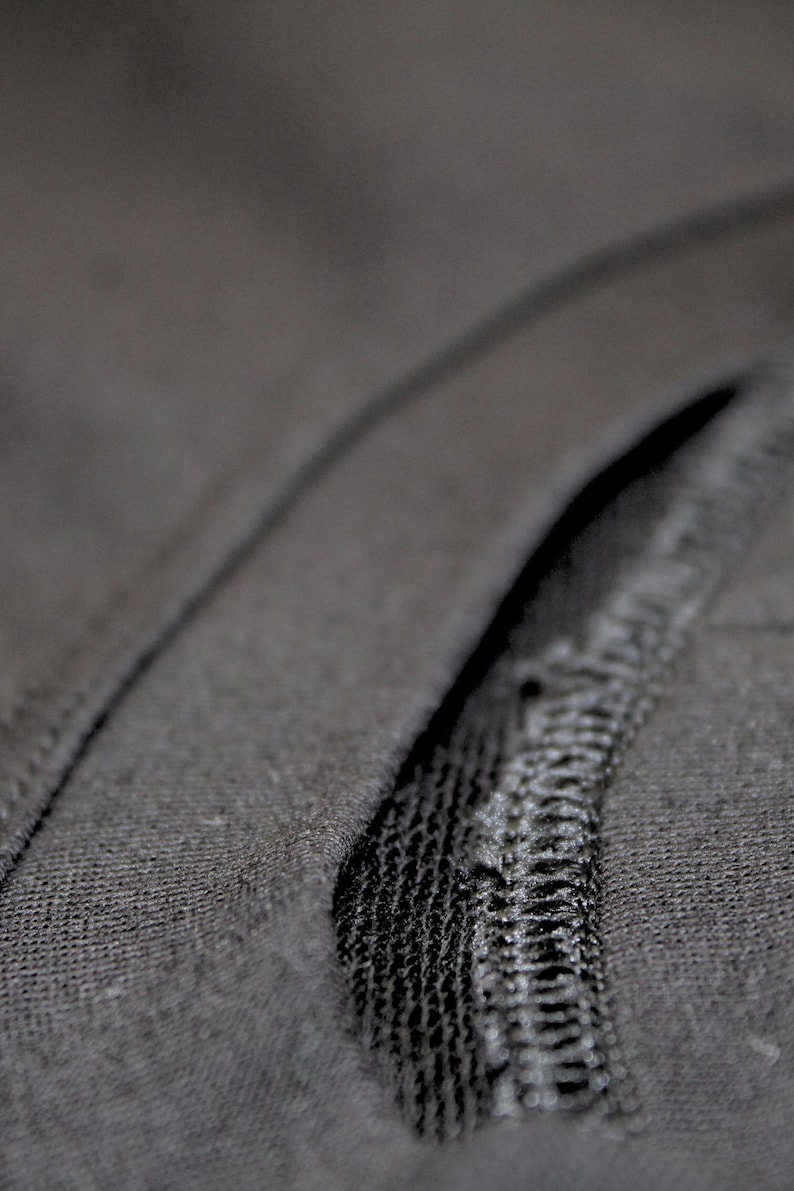 May include: Close-up of dark gray fabric with a visible seam. The fabric appears to be a soft knit material. The seam is stitched with a contrasting thread, creating a textured detail.