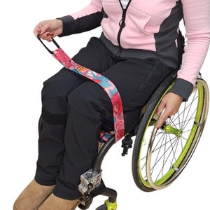 Könnte beinhalten: Eine Person in einem Rollstuhl mit einem floral gemusterten Transfergurt. Der Gurt ist am Rollstuhl befestigt und hat einen Griff für einen einfachen Transfer.