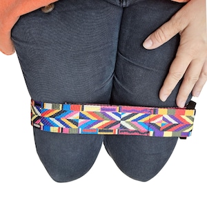 Peut inclure: Une sangle en tissu à motifs colorés avec une bordure noire. La sangle est enroulée autour d'une paire de jambes en jean.