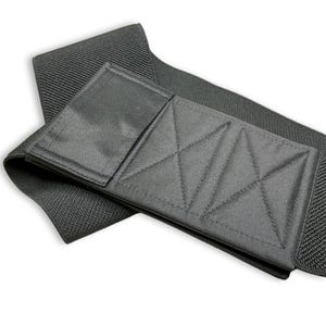 May include: A black, padded shoulder strap with a textured, woven strap and a rectangular pad with diamond stitching. The pad has a flap that folds over the strap. The strap is designed to be worn over the shoulder.