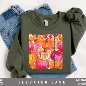 A green sweatshirt with a vibrant pumpkin graphic printed on it, along with a pair of blue jeans.