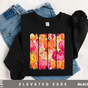 A black t-shirt with a vibrant graphic design of colorful pumpkins on it, along with a pair of blue jeans.