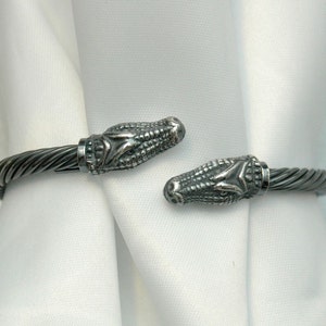 May include: A silver bracelet with alligator head ends. The bracelet is made of twisted wire.