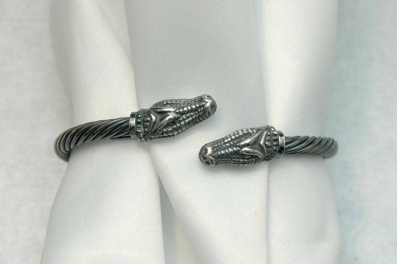 May include: A silver bracelet with alligator head ends. The bracelet is made of twisted wire.
