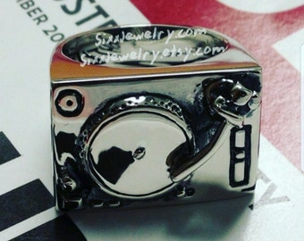 May include: A silver ring shaped like a turntable with a record on it. The ring is a detailed replica of a classic turntable.