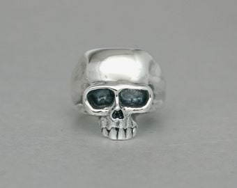 May include: A silver skull ring with a detailed design. The ring is made of polished silver and has a realistic skull design.