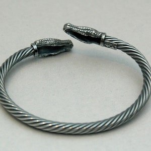 May include: A silver bracelet with a twisted cable design and alligator head clasps.