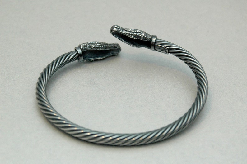 May include: A silver bracelet with a twisted cable design and alligator head clasps.