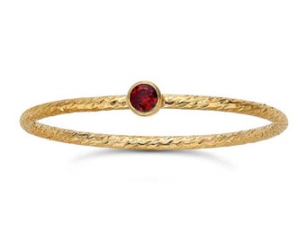 May include: A gold ring with a textured band and a single red gemstone.