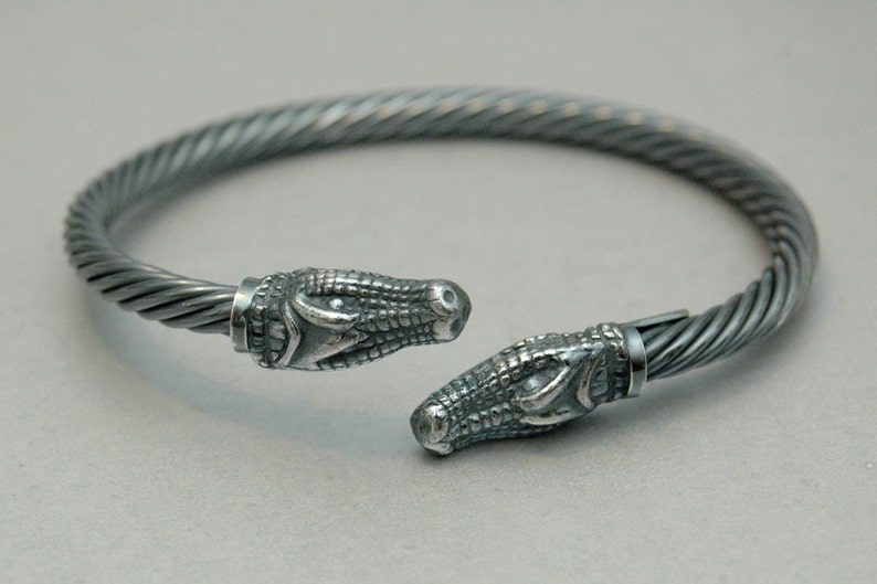 May include: A silver bracelet with a twisted cable design and alligator head ends.