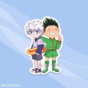 May include: A sticker depicting two anime-style characters. One has white hair and blue eyes, holding a yellow and orange object. The other has green hair and is wearing a green outfit, giving a peace sign. The sticker has a white border and a light blue background.
