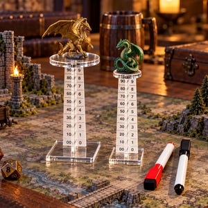 May include: Two clear acrylic vertical tracking towers with square bases and circular platforms. Each tower features a printed scale from 00 to 90 and 0 to 9. A gold dragon figurine stands on the taller tower, and a green dragon figurine on the shorter.