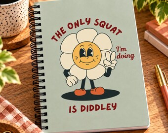 May include: A spiral-bound notebook with a light green cover featuring a cartoon flower character with a yellow face and white petals. The text reads THE ONLY SQUAT I'm doing IS DIDDLEY in red letters. The character is making a peace sign gesture.