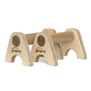 Può includere: Un paio di parallele in legno con finitura naturale. Le parallele sono realizzate in legno massello e hanno una forma arrotondata. Le parallele sono montate su due basi in legno con il logo Jumpbox stampato su ciascuna base.