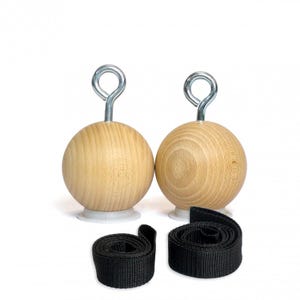 Op de afbeelding: Twee houten grijpballen met metalen oogjes en zwarte nylon banden. De lichtbruine bollen staan op witte voetjes. De banden zijn opgerold. De items zijn voor krachttraining en fitness.