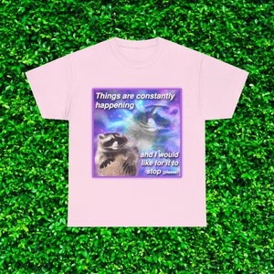 May include: Pink t-shirt with a graphic of two raccoons in a galaxy background. The text reads "Things are constantly happening and I would like for it to stop (please)"