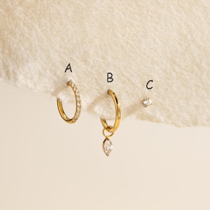 May include: Three gold-toned earrings labeled A, B, and C. Earring A is a small hoop with embedded clear stones. Earring B is a plain gold hoop with a dangling marquise-cut clear stone charm. Earring C is a single small stud with a clear stone.