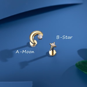 May include: Two gold-colored earrings, one shaped like a crescent moon and the other a star. Both earrings have a small, clear gemstone. The text "A-Moon" and "B-Star" are written on the image.