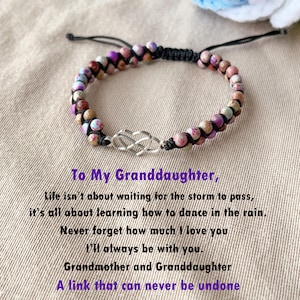 Könnte beinhalten: Ein Armband aus Perlen mit einem silbernen Unendlichkeits-Anhänger. Das Armband besteht aus bunten Perlen und einer schwarzen Schnur. Der Text "To My Granddaughter, Life isn't about waiting for the storm to pass, it's all about learning how to dance in the rain. Never forget how much I love you I'll always be with you. Grandmother and Granddaughter A link that can never be undone" steht unter dem Armband.