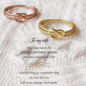 May include: Two rings, one rose gold and one gold, with a knot design and small clear stones. The rings are on a white, textured surface. Text reads "To my wife" and "EVERLASTING BOND".