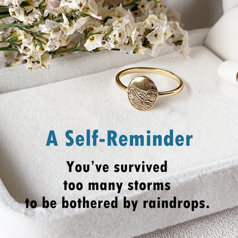 May include: A gold ring with a wave design on the band. The ring is in a white box with the text "A Self-Reminder You've survived too many storms to be bothered by raindrops."