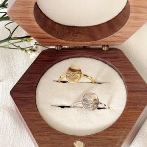 May include: Two rings with wave designs in a wooden box. One ring is gold and the other is silver.