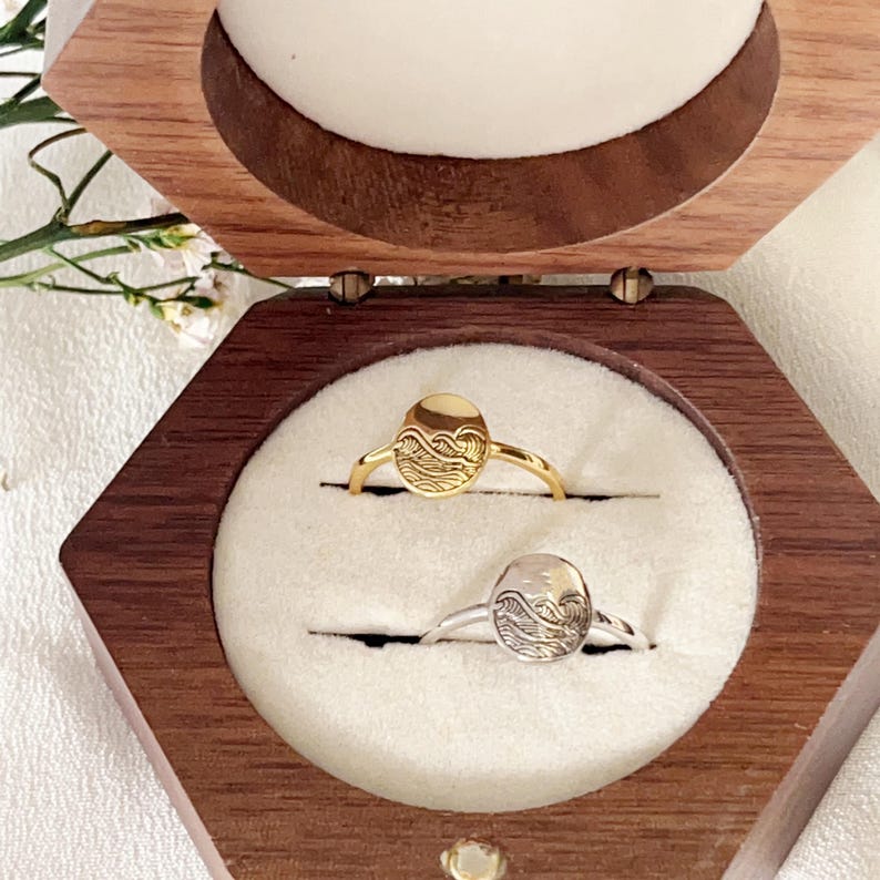 May include: Two rings with wave designs in a wooden box. One ring is gold and the other is silver.