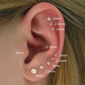 May include: An ear with several gold stud earrings of different sizes, from 2mm to 4mm in diameter. The sizes are labelled in millimetres next to each earring, showing a variety of options for ear piercing jewellery.