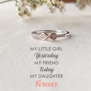 May include: A silver infinity ring with small clear stones set in the band. The ring is on a white background with the text "My little girl Yesterday My friend Today My daughter Forever".