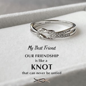 May include: A silver ring with a knot design and small clear stones. The ring is in a white box with the text "My Best Friend OUR FRIENDSHIP is like a KNOT that can never be untied".