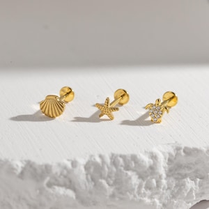May include: Three gold-tone stud earrings featuring ocean-themed designs. One earring is shaped like a seashell, one is a five-pointed starfish, and the third is a sea turtle with small clear stones embedded in its shell on a flat back post.