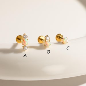 May include: Gold-toned stud earrings with opal and clear crystal accents. The earrings are available in three different designs, labeled A, B, and C. The opal stones have a pearlescent, iridescent quality.