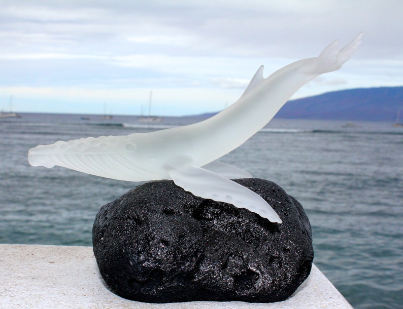 Pu&ograve; includere: Una scultura in vetro trasparente di una megattera che salta fuori dall'acqua, appoggiata su una roccia di lava nera. La scultura &egrave; una bellissima rappresentazione della bellezza dell'oceano.