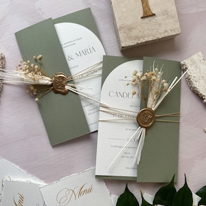 Op de afbeelding: Olijfgroene trouwuitnodigingen met gouden folie accenten, vastgebonden met touw en versierd met gedroogde bloemen en zegelwas. Inclusief menukaarten en een tafelnummer. De uitnodigingen luiden "& MARIA" en "CANDELA".