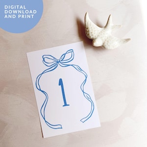 Puede incluir: Tarjeta de número de mesa imprimible azul y blanca con un lazo de cinta azul y el número "1" en el centro.