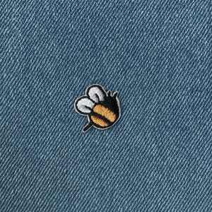 Könnte beinhalten: Gestickter Bienen-Aufnäher mit schwarzen, weißen und gelben Details, vor blauem Denim-Hintergrund. Das Etsy-Logo ist oben mittig sichtbar. Dieser Aufnäher ist für Kleidung oder Accessoires geeignet.