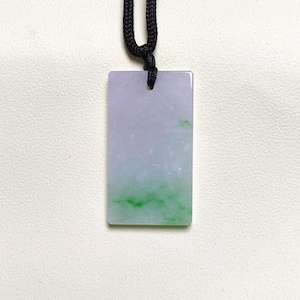 May include: A rectangular jade pendant with a gradient of lavender and green hues, suspended from a black cord. The polished stone displays a natural, translucent appearance, showcasing the unique color variations.