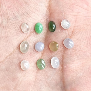 May include: A collection of eleven small, smooth, oval-shaped cabochon gemstones in various colors including translucent white, light green, dark green, pale lavender, and soft yellow, all featuring a polished, reflective surface finish.