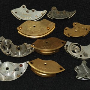 May include: A collection of 10 metal watch parts, some are gold-coloured and some are silver-coloured. The parts are various shapes and sizes, some are round, some are crescent-shaped, and some are rectangular.