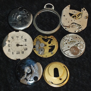 May include: A collection of disassembled vintage pocket watch parts, including a silver bezel, a watch face with black numerals, and various gears and plates. The components are arranged on a dark surface, revealing the intricate mechanics.