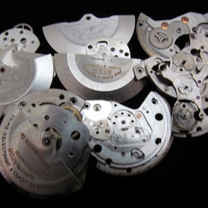 May include: A selection of dismantled watch components, including gears, plates, and balance wheels, set against a black backdrop. Some parts are stamped with text, such as "Caravelle Watch" and "Unadjusted Swiss Dynator". The components are silver-toned.