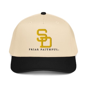 Puede incluir: Gorra de béisbol con corona color crema y visera negra. La gorra presenta un logotipo "SD" dorado bordado y el texto "FRIAR FAITHFUL" en negro. La gorra tiene una visera curva y un botón negro en la parte superior.