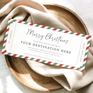 May include: A rectangular Christmas gift certificate with red and green striped borders, on a wooden plate and a beige cloth. The text reads "Merry Christmas" and "Your Destination Here."