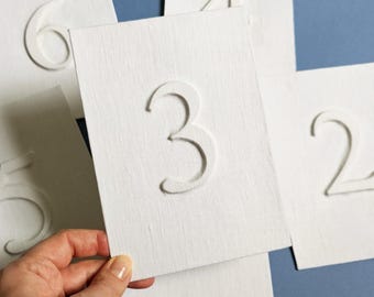 Números de mesa de lino para bodas, tela con aspecto de relieve 3D, color blanco natural y azul salvia.