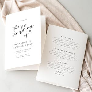 Könnte beinhalten: Eine weiße Hochzeitseinladungskarte mit schwarzem Text. Die Karte lautet "Willkommen zur Hochzeit von Mia Catherine und William John" und enthält Datum, Uhrzeit und Ort der Hochzeit. Die Rückseite der Karte enthält Informationen über den Empfang, einen Abschnitt über liebevolle Erinnerungen und eine Dankesbotschaft.
