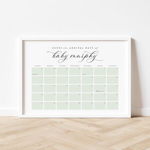 May include: A framed calendar print with the text "Guess the arrival date of baby murphy" in elegant script. The calendar grid features pale green squares and dates for September and October. The frame is white.